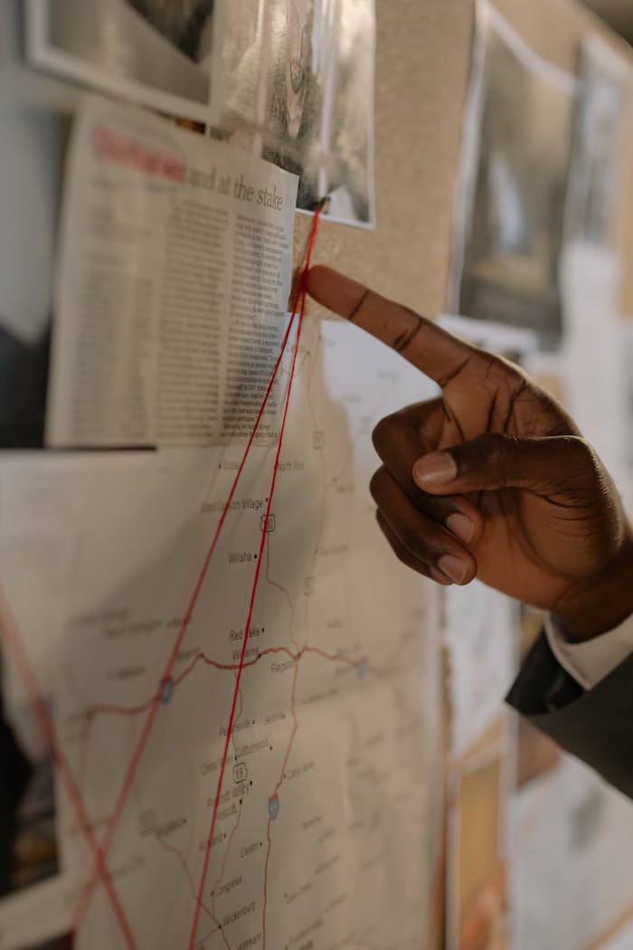 services-02 A hand pointing at a map with red strings on a corkboard, depicting an investigation setup.